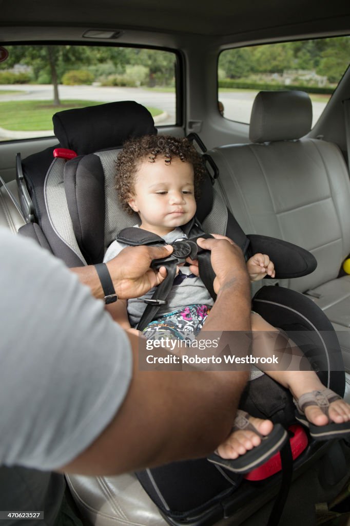 Father buckling toddler son into car seat