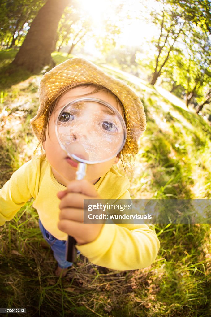 Funny curious toddler holding magnifying glass up to her face