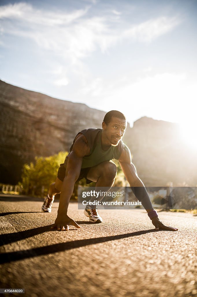 Determined African American runner in starting position on a roa