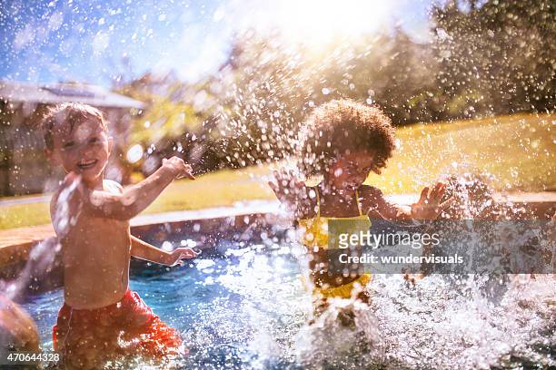 poco chica afro y amigo salpicaduras de agua en la piscina - water garden fotografías e imágenes de stock
