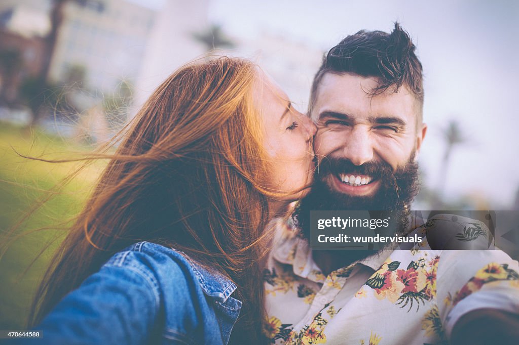 Girl kissing her smiling hipster boyfriend on his cheek