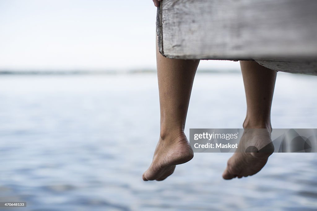 Low section of woman dangling feet from pier