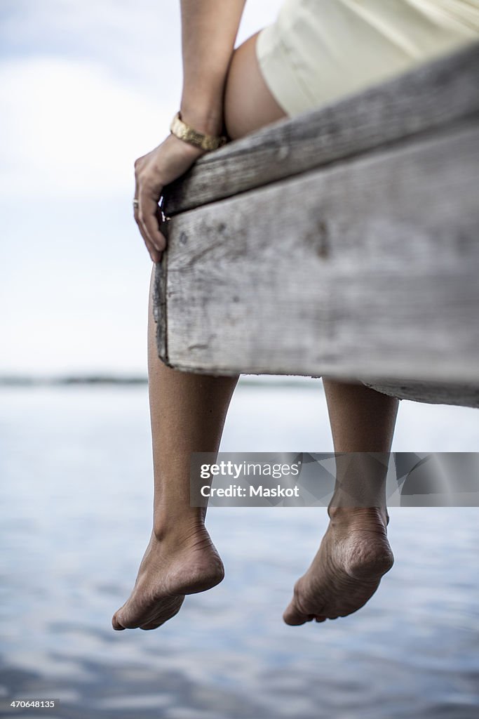 Low section of woman dangling feet from pier