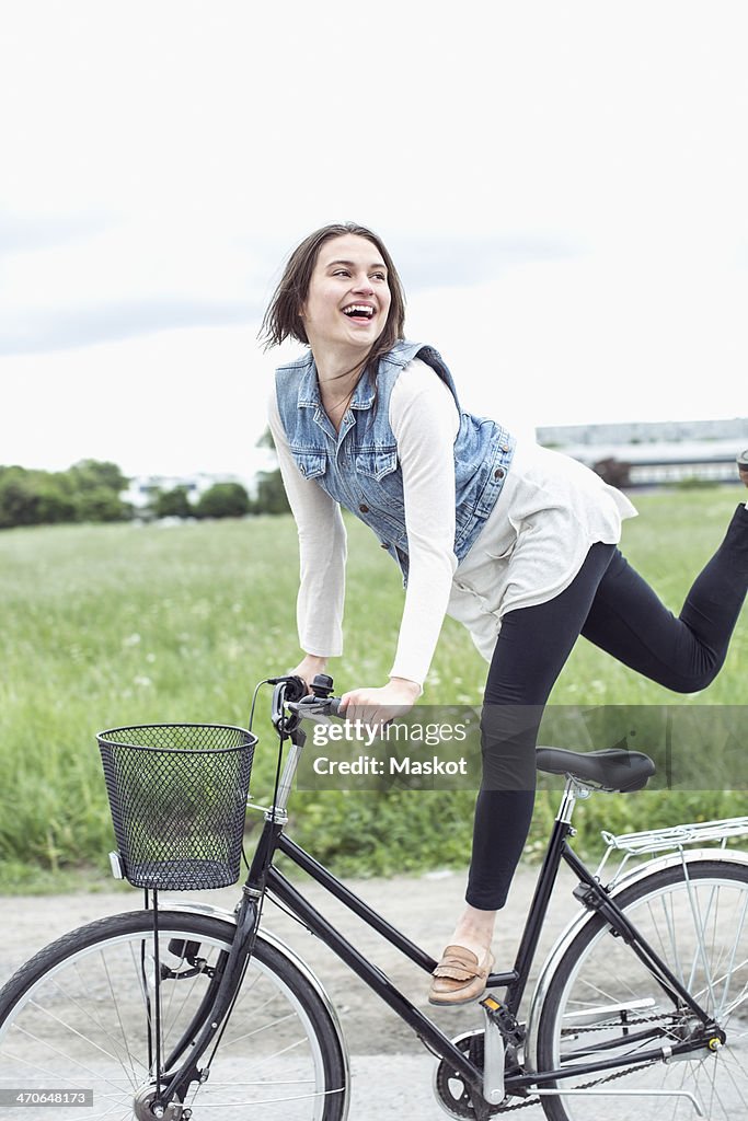 Happy young woman performing trick on bicycle at countryside