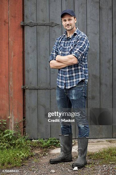 full length portrait of confident farmer standing arms crossed against barn - farm worker foto e immagini stock