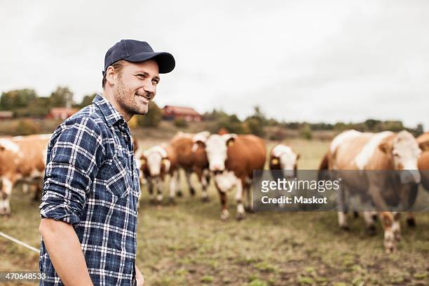 smiling farmer looking away at field while animals grazing in background - cow stock-fotos und bilder