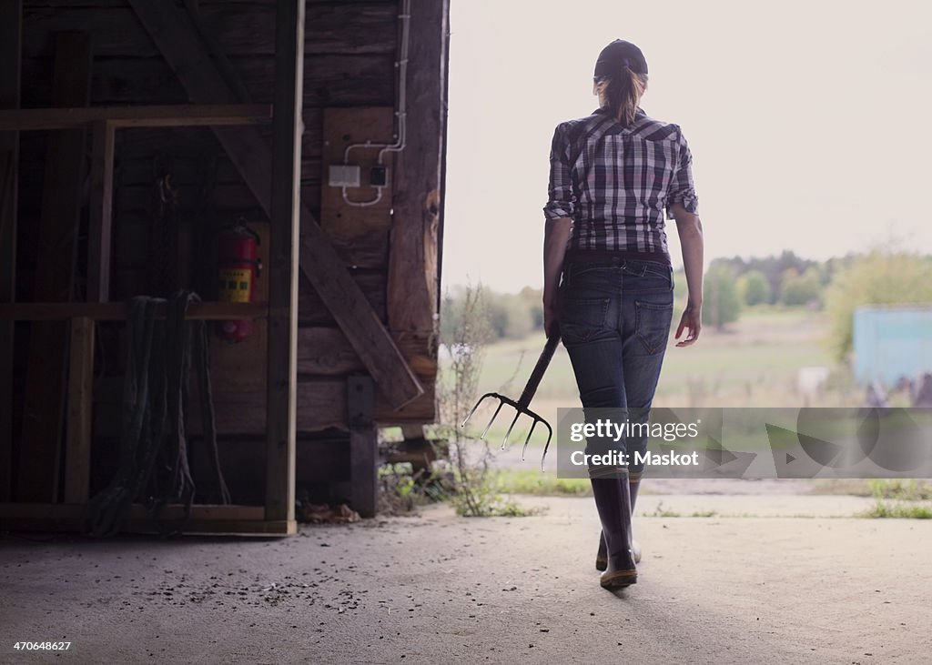 Rear view of female farmer with pitchfork walking in barn