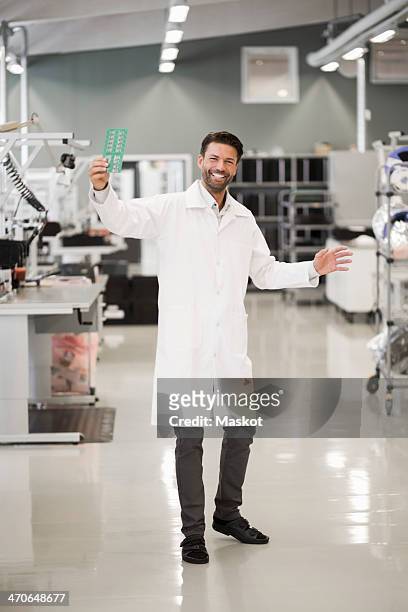 full length portrait of happy engineer showing machine part in manufacturing industry - laborkittel stock-fotos und bilder