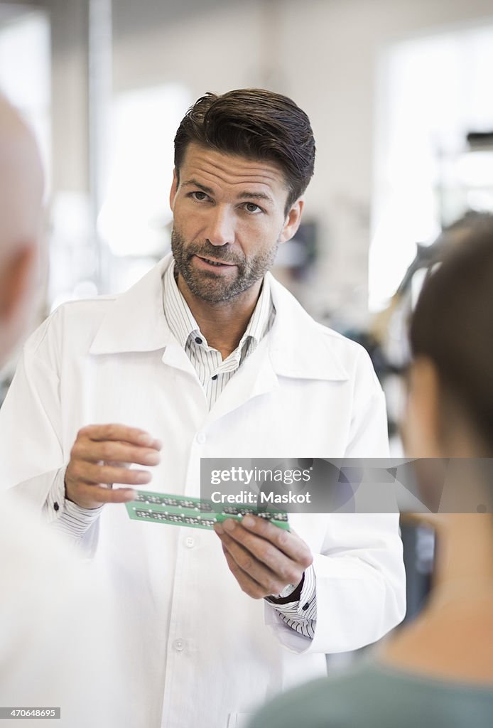 Male engineer explaining circuit board to business people in factory