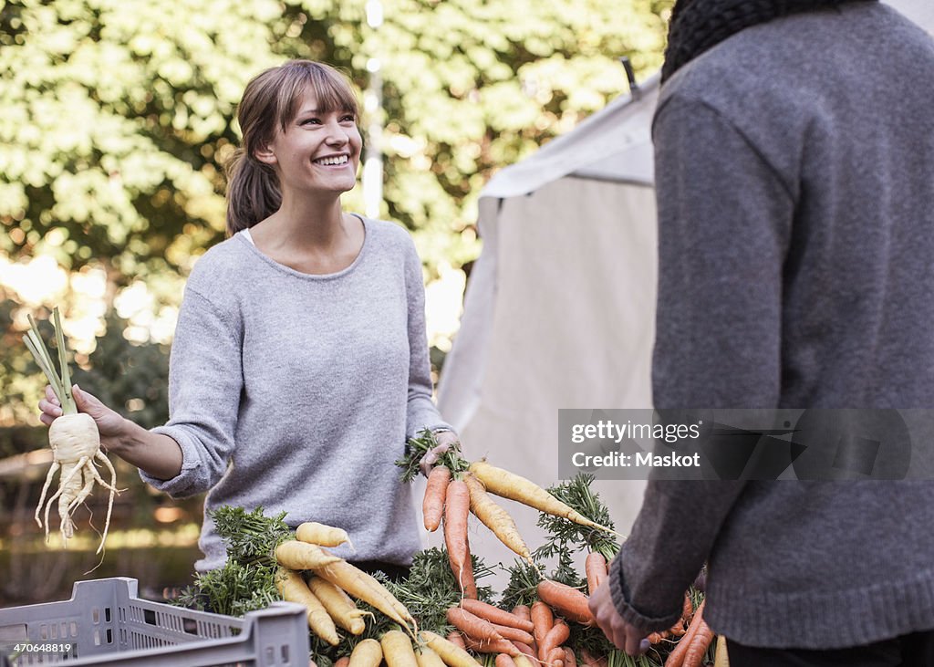 Young female vendor selling vegetables at market stall