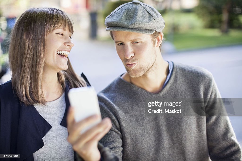 Happy couple photographing themselves through mobile phone outdoors