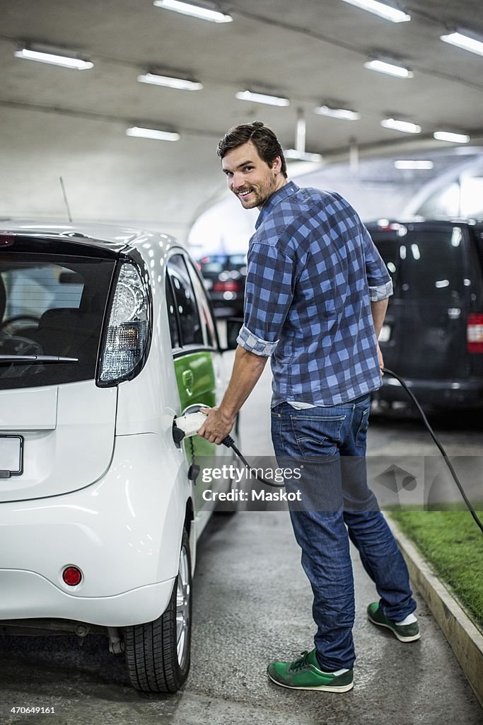Full length portrait of young man charging electric car at gas station
