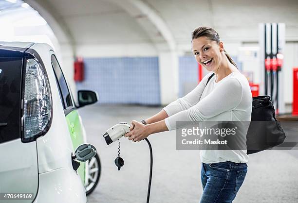 side view portrait of playful woman electrical charger pump at gas station - electric car charger imagens e fotografias de stock