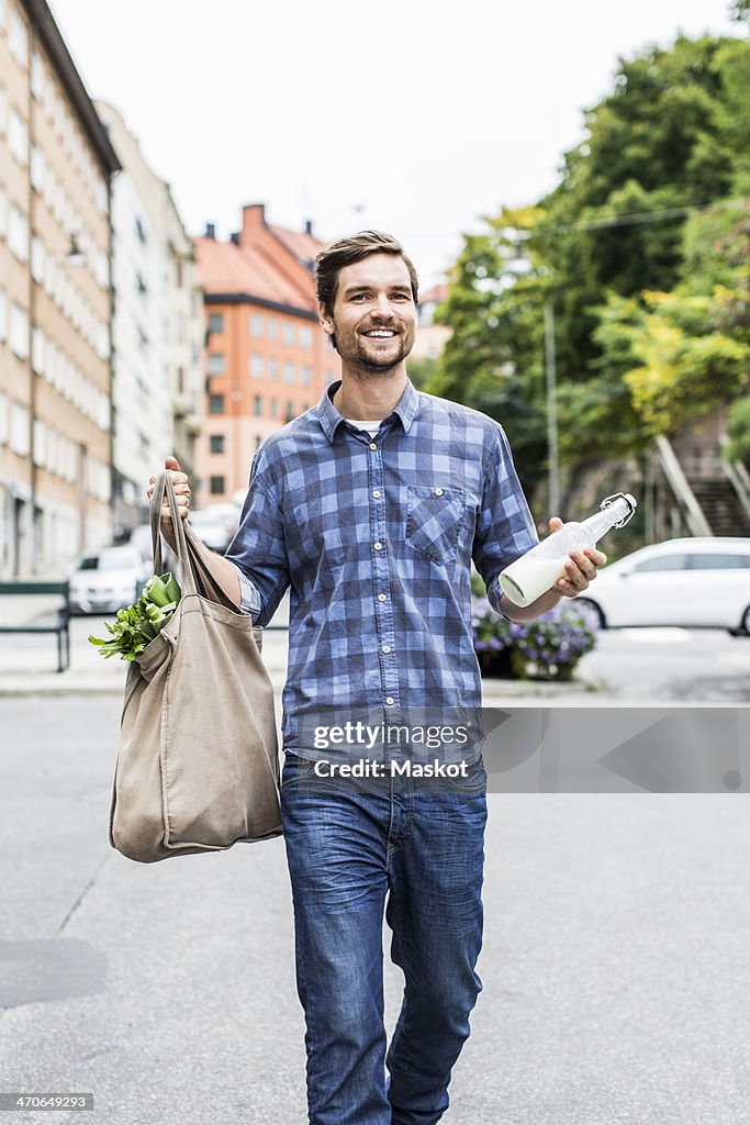 Full length portrait of happy man with groceries walking on street