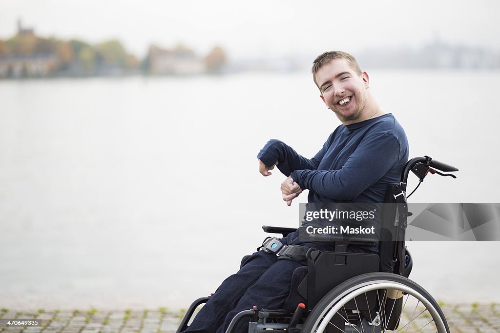 Portrait of happy man with cerebral palsy sitting on wheelchair by lake