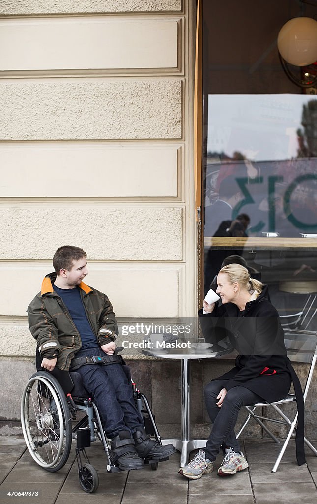 Female caretaker and disabled man having coffee at sidewalk cafe