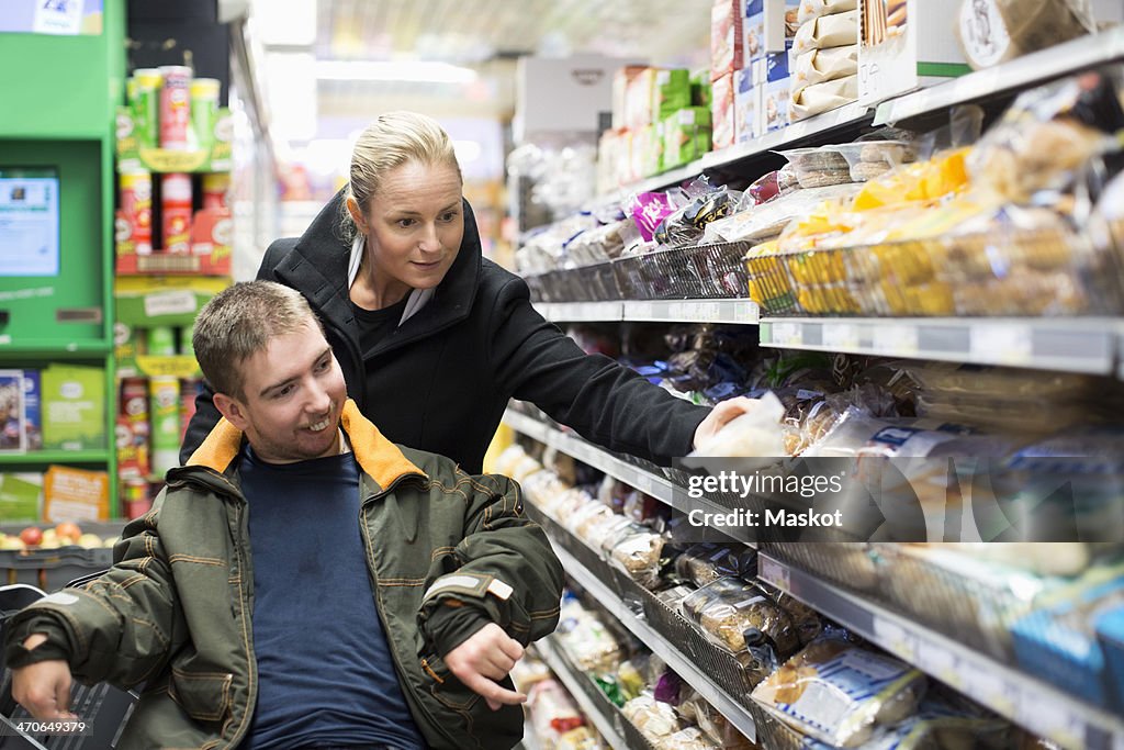 Caretaker shopping with disabled man on wheelchair in supermarket