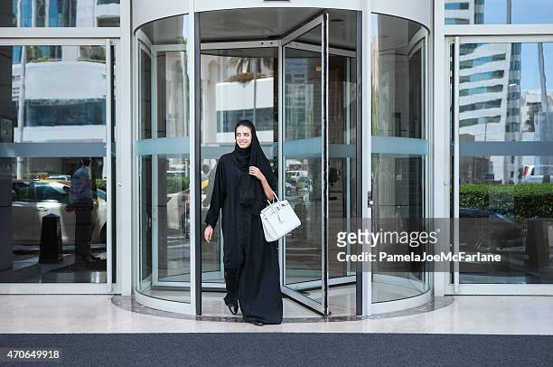 smiling, young emirati woman in abaya leaving modern luxury hotel - city walk dubai stockfoto's en -beelden