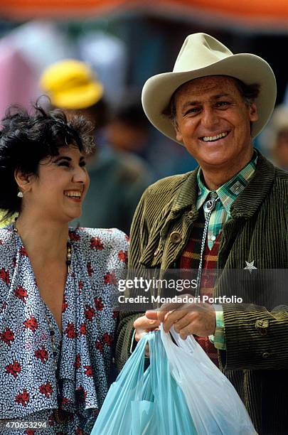 "The fanciful artists Renzo Arbore and Marisa Laurito joke and laugh, while he keeps some shopping bags; the two artists are working around the...
