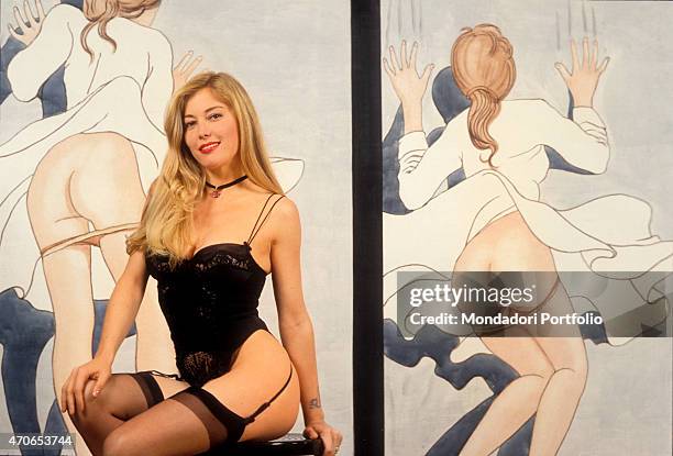 "Moana Pozzi in lingerie and suspenders, posing against the painted backdrop in the offices of Diva Futura, the agency of her manager Riccardo...