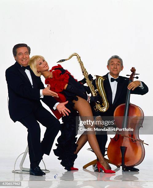 Host Corrado and composer Roberto Pregadio sit on stools wearing a tuxedo to promote the variety show ""La corrida""; between them, showgirl...