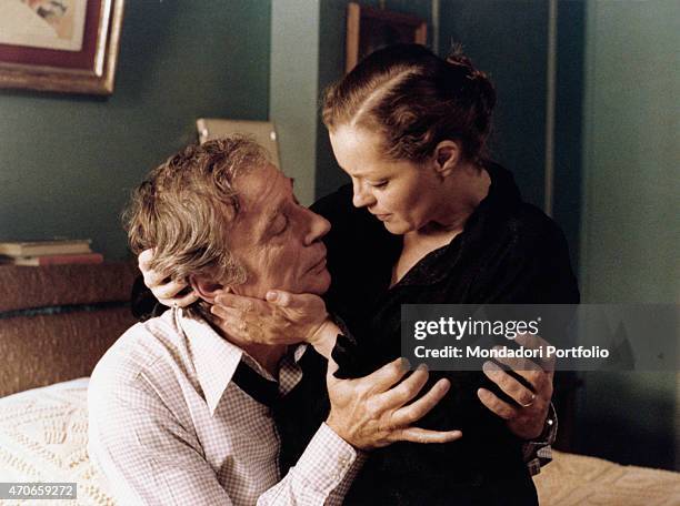 "The French actors Yves Montand and Romy Schneider hold theirselves intensely looking at each other with a deep glance sitting on the bed; the two...
