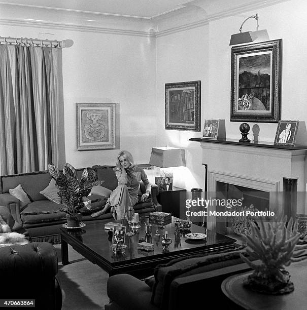 "Virna Lisi in her living room, seated on a sofa, below a Campigli painting and by the fireplace; a photo of her with husband Franco Pesci is placed...