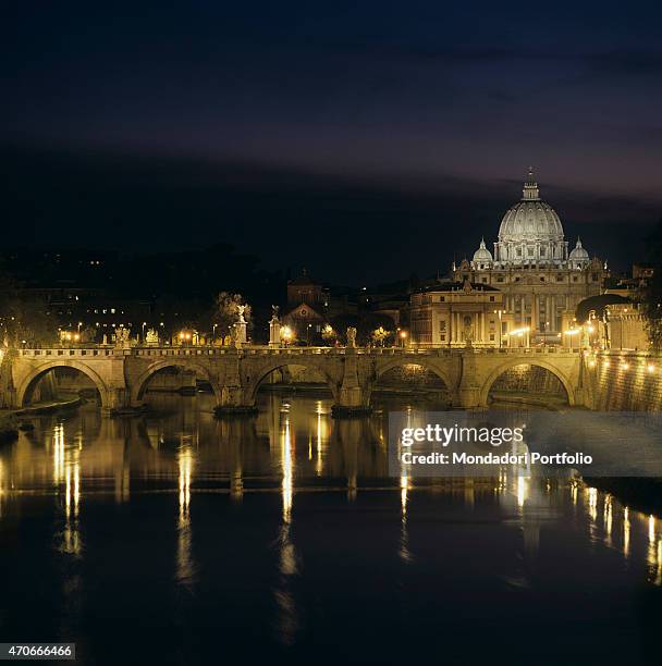 "View of the Eternal City by night: the Tiber river, whose water surface reflects the lamps of Ponte Sant'Angelo, and, in the background, the famous...