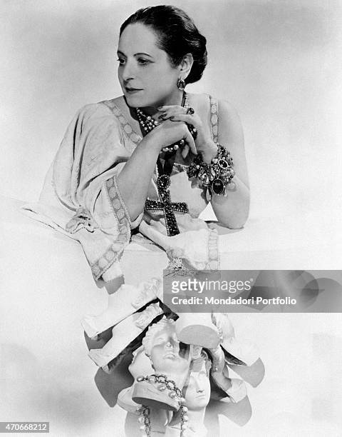 "Cosmetics entrepreneur Helena Rubinstein taken in an elaborate photographic composition, leaning on a white base and gazing pensively towards the...