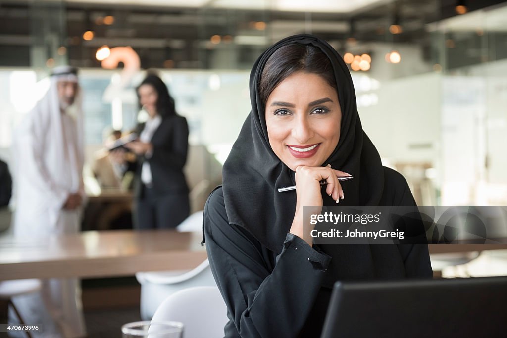 Arabi sorridente donna d'affari che tiene una penna in ufficio