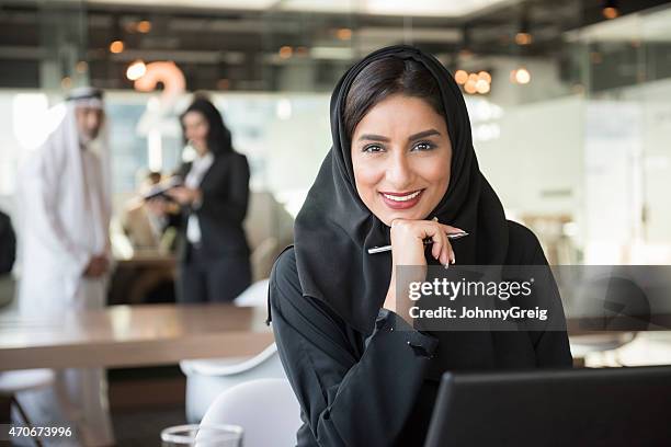 arabi sorridente donna d'affari che tiene una penna in ufficio - emirati at work foto e immagini stock