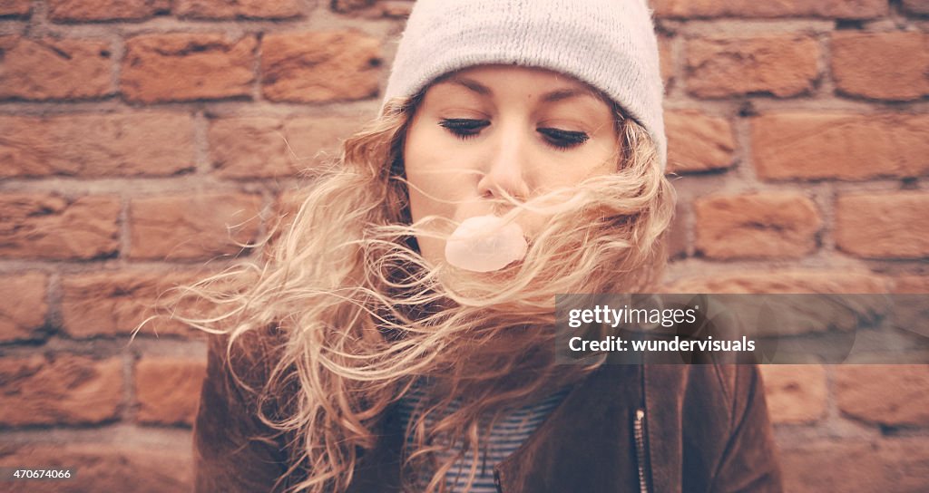 Girl blowing bubble gum with a brick wall behind her