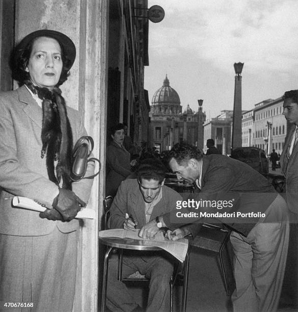 Man filling the natural persons' annual income declaration form seated at the table of a caf on via della Conciliazione. Rome, 1950s "