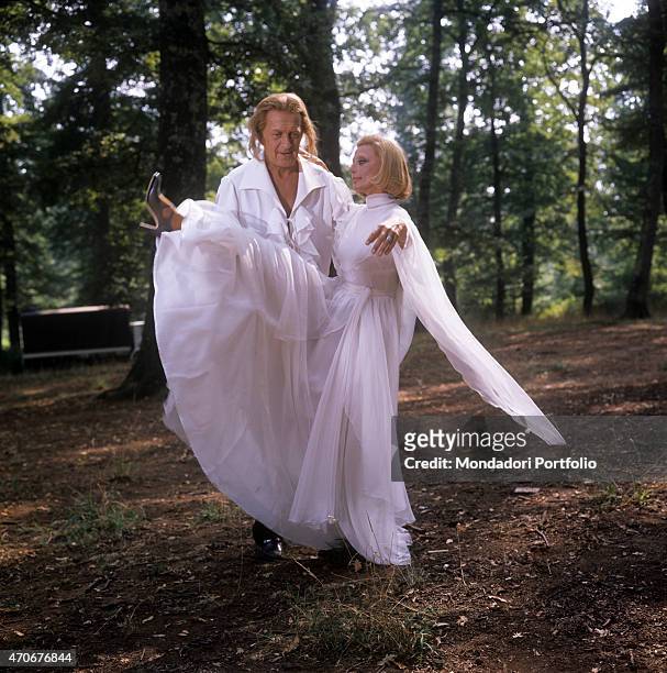 "Italian actress and TV presenter Sandra Mondaini in a white dress lifting her leg helped by her husband and Italian TV host Raimondo Vianello...