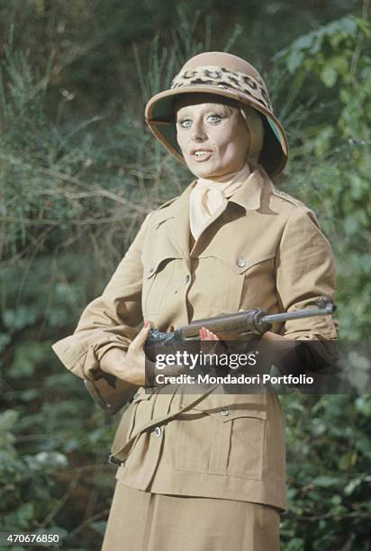 "Italian actress and TV presenter Sandra Mondaini acting in the final theme of the TV variety show Noi no with a rifle in the hands. Italy, 1977 "