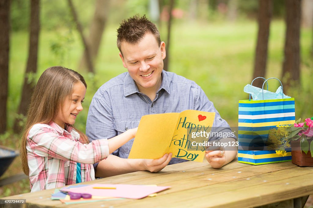 Daughter shows dad handmade Father's Day card. Outdoors. Child, parent.