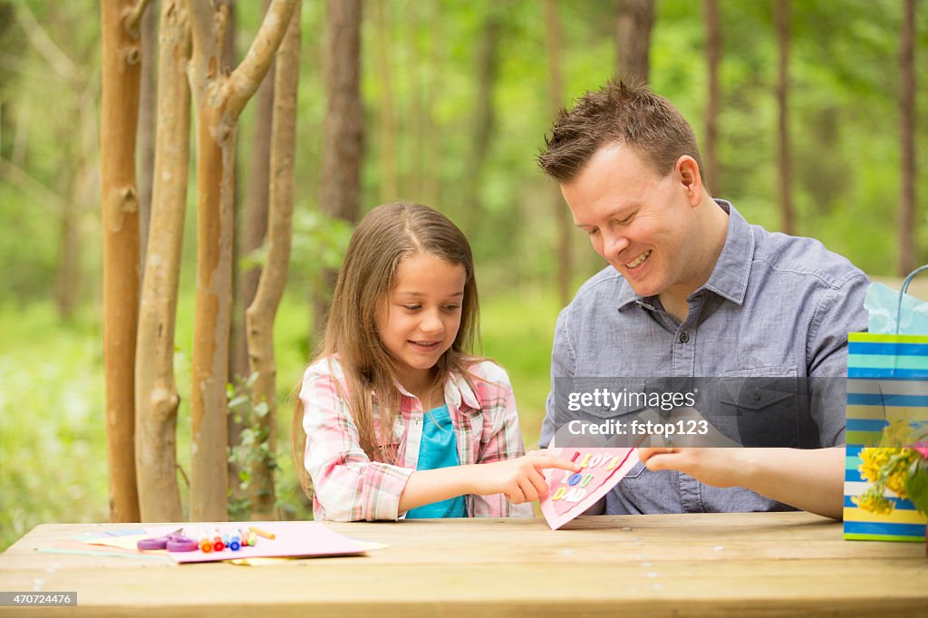 Daughter shows dad handmade Father's Day card. Outdoors. Child, parent.