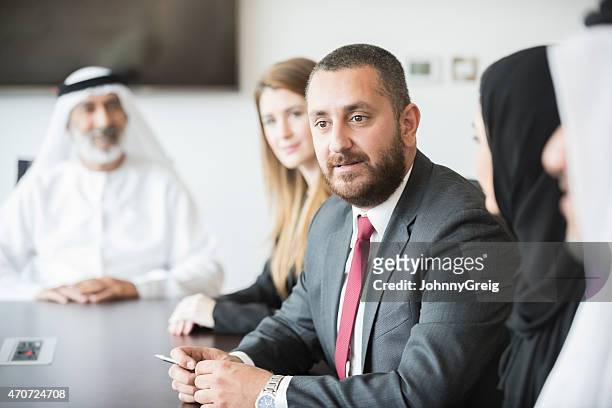 middle eastern businessman with colleagues at conference table - west asia stock pictures, royalty-free photos & images