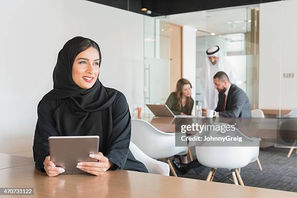 geschäftsfrau hält digitale tablet beim wegsehen - emirati at work stock-fotos und bilder
