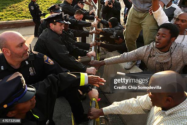 Demonstrators and police officers wrestle over a metal barricade during a protest against police brutality and the death of Freddie Gray outside the...