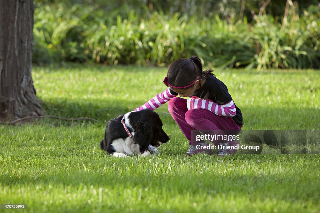 Young girl petting a dog laying on the grass.