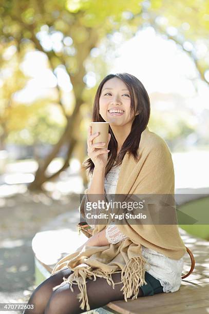 woman drinking coffee sitting on park bench - shawl foto e immagini stock