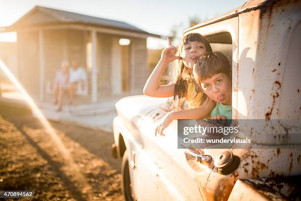 children pulling faces while their grandparents sit on porch behind - old brother stock pictures, royalty-free photos & images