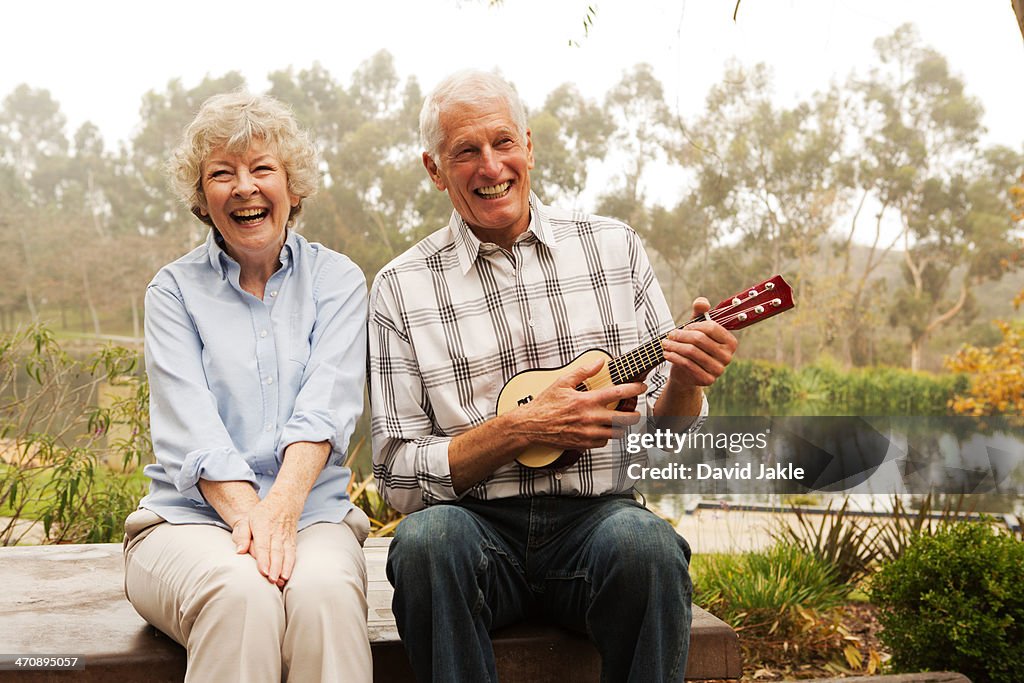 Husband playing the ukulele with wife by lake