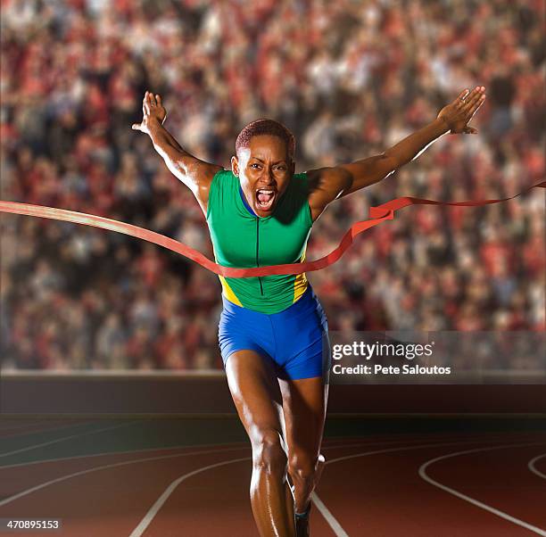 young woman sprinting through winners tape in stadium - short track imagens e fotografias de stock