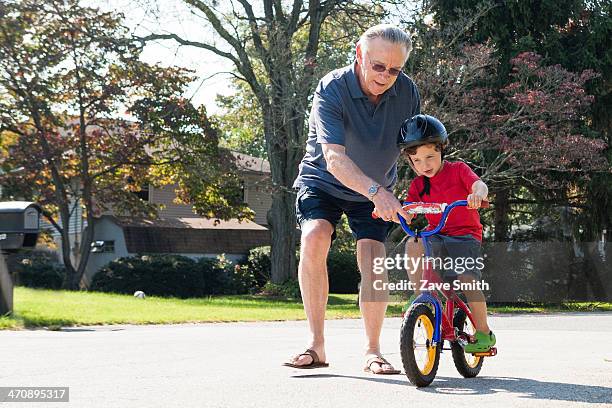 grandfather encouraging young boy to ride bicycle - house old bike stock-fotos und bilder