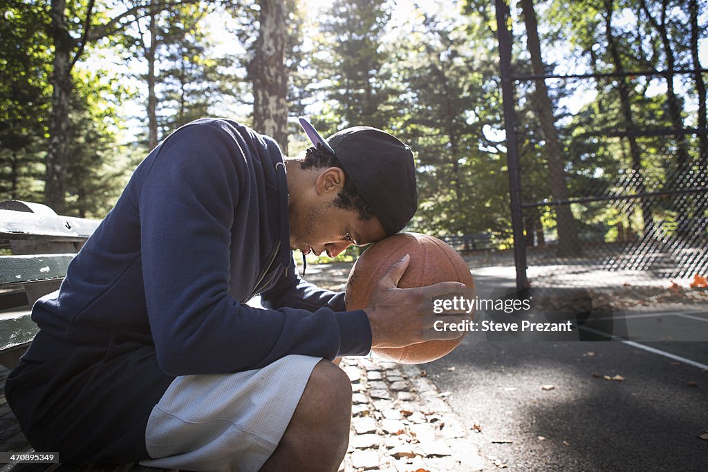 Young man sitting on park bench resting head on basketball