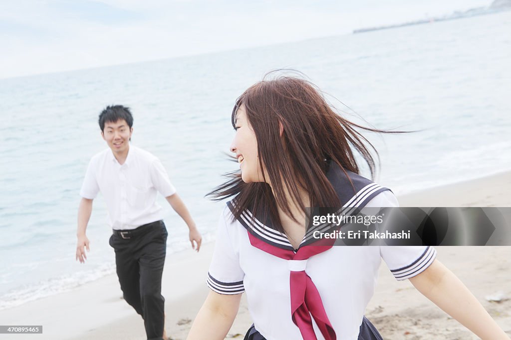 Young couple wearing school uniform running on sandy beach