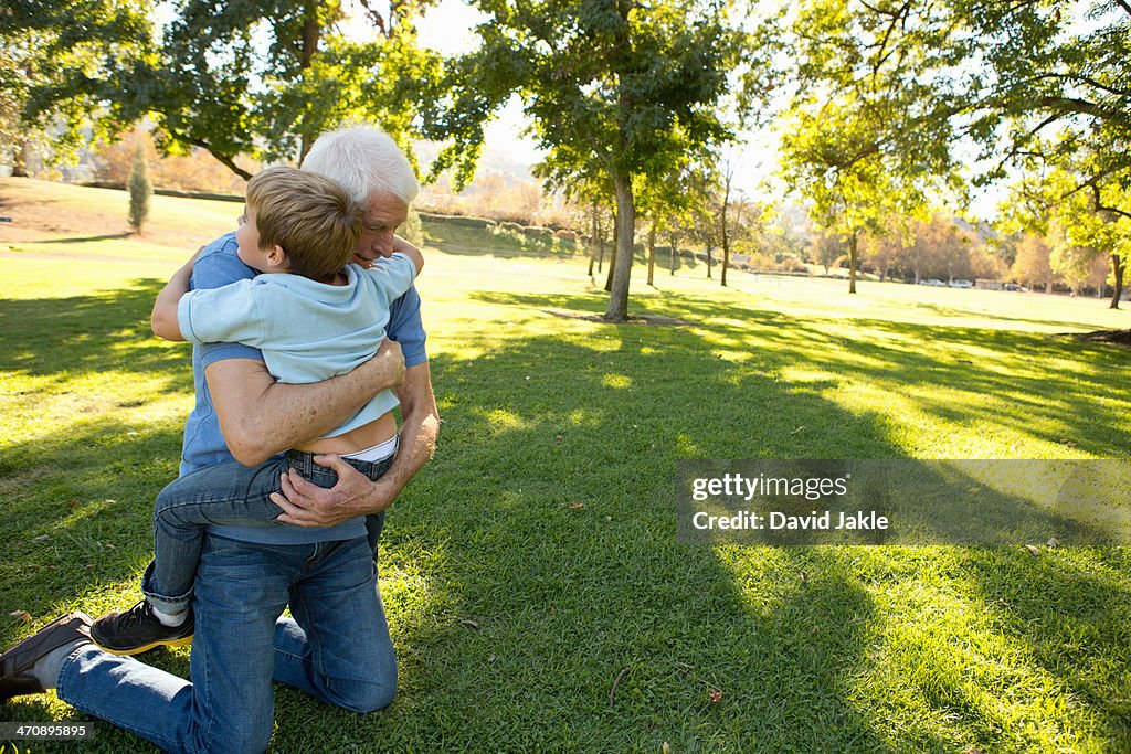 Grandfather kneeling on grass hugging grandson