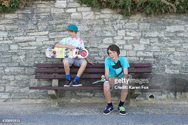 portrait of two boys sitting on bench holding skateboards - teenagers only stock pictures, royalty-free photos & images